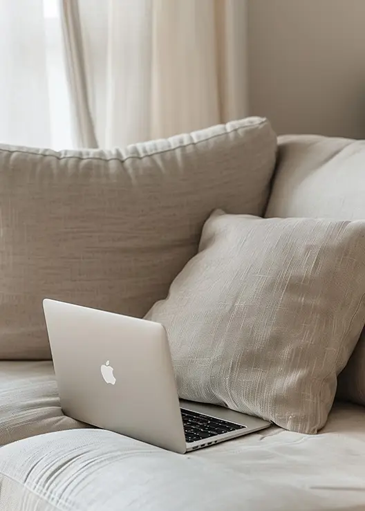 MacBook Laptop on a comfy beige couch in a soft, light-filled space