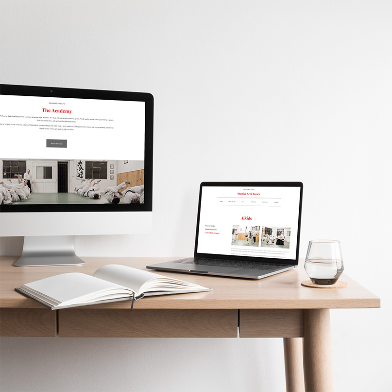Martial arts website displayed on desktop and laptop with open notebook on wooden desk