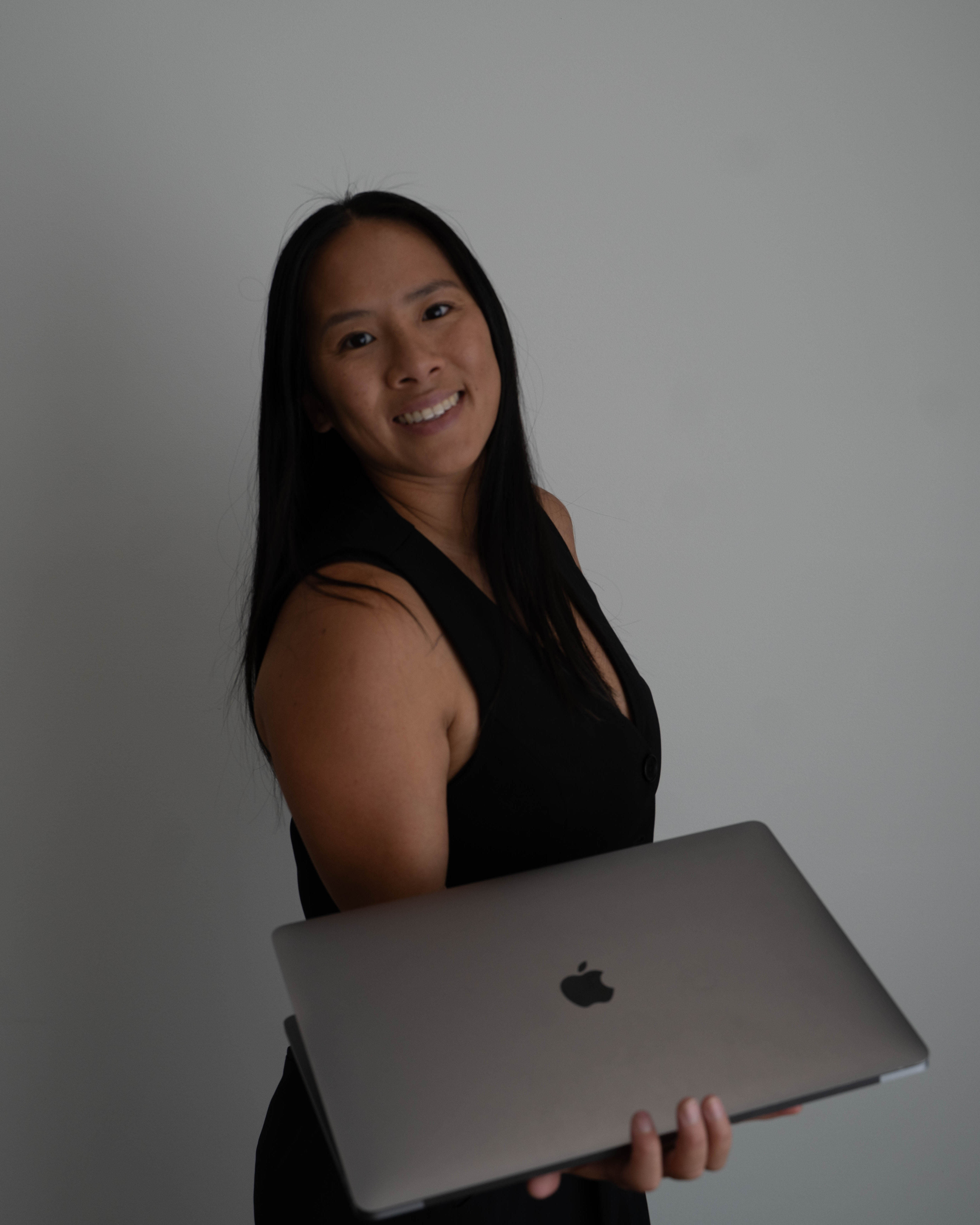 Candid portrait of designer Tina Jenner holding laptop, smiling at camera, professional approachable headshot for design studio founder.