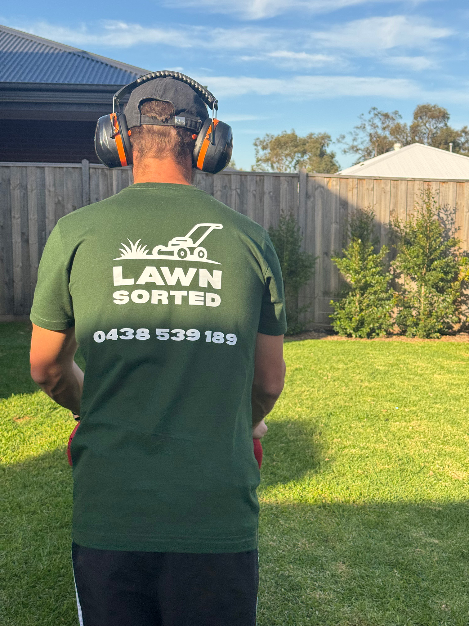Lawn Sorted team member wearing branded green t-shirt with logo and phone number on job site, showing mobile brand presence